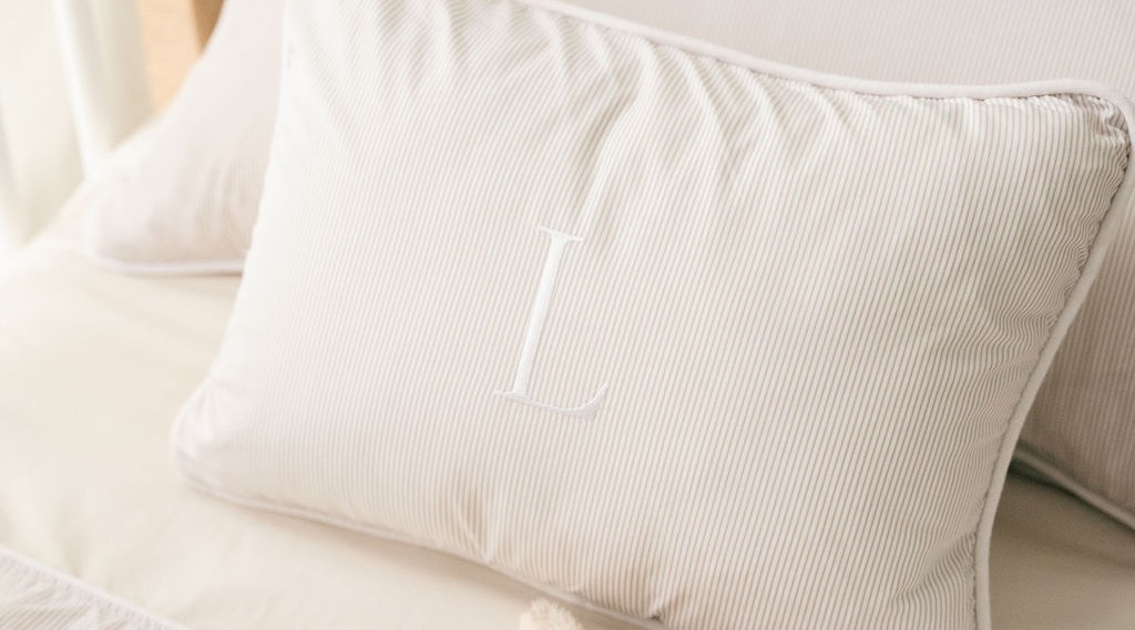 Personalised accent pillow with an embroidered monogram letter resting on striped bedding